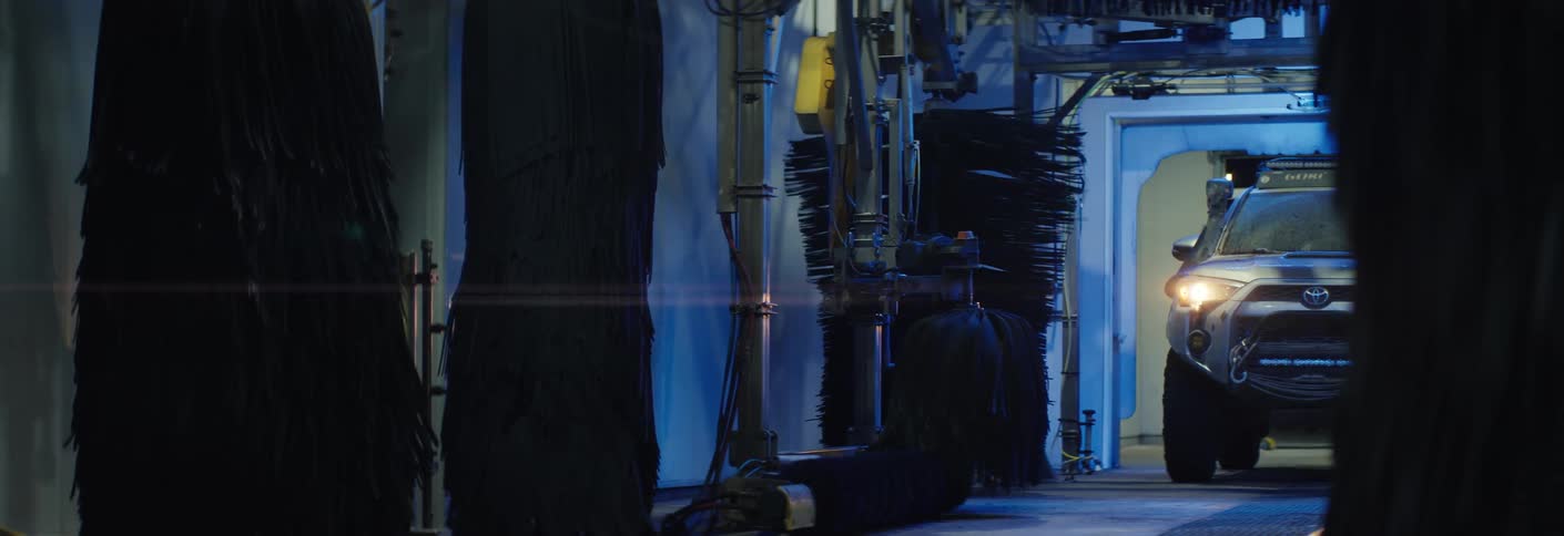 A vehicle begins driving down the inside of a car wash bay the brushes are rolling as the suv moves forward
