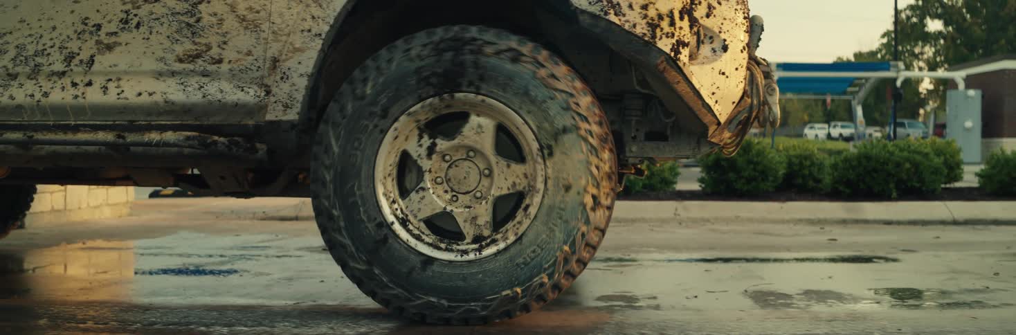 A muddy off road vehicle tire rolls slowly across a wet parking lot surface