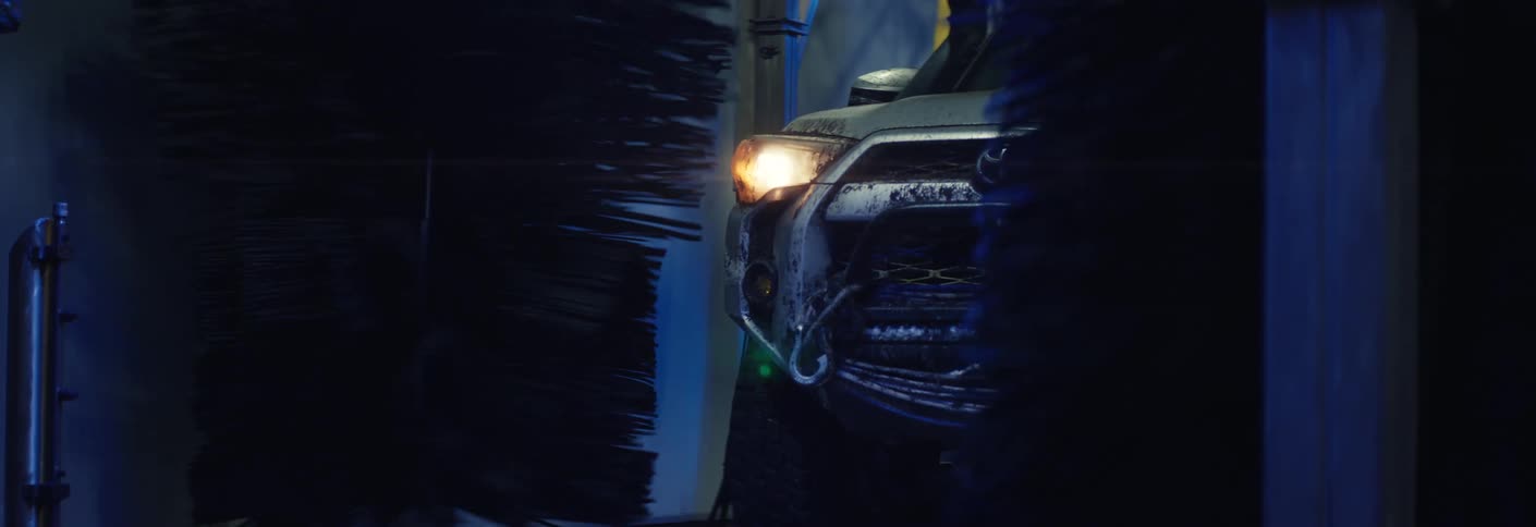 A car driving into a car wash at night as the sponges spin during the process