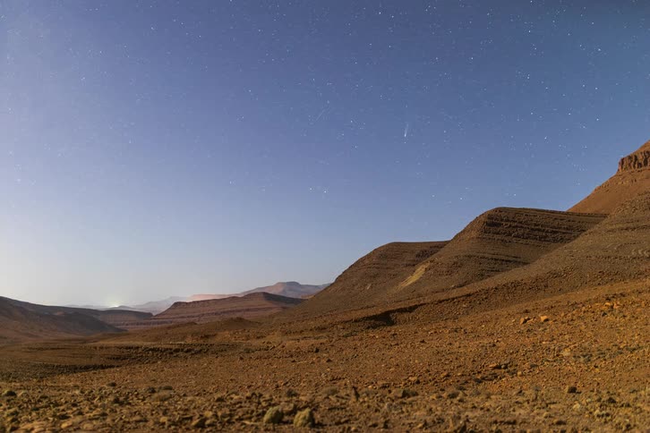 Desert landscape with rocky mountains under a starry sky at dawn