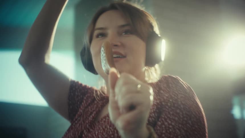 A housewife singing enthusiastically into a wooden spoon while dancing joyfully in a kitchen