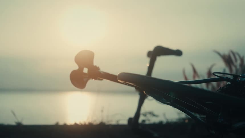 A lone bicycle rests in silhouette by the water as the sun sets capturing a quiet moment