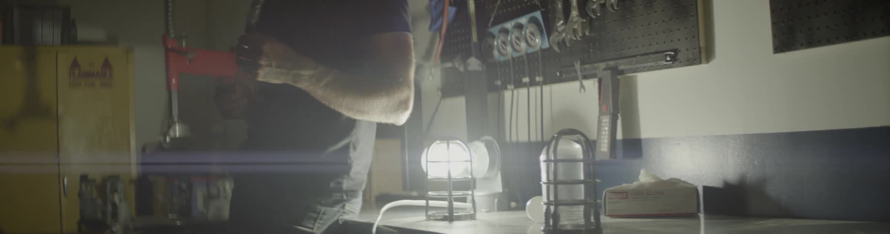 A man stands holding a tool in a workshop