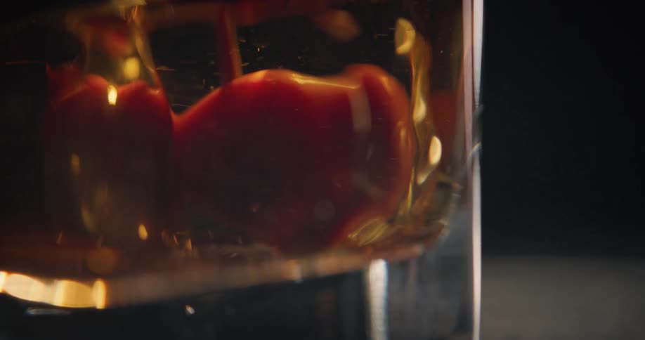 A closeup shot shows a red cherry being dropped into a glass of dark amber liquid the fruit settles at the bottom of the glass as small bubbles rise through the drink