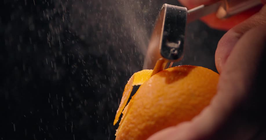 Closeup hands of a person peeling orange zest with a tool