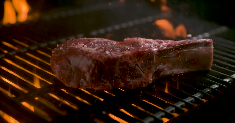 Closeup of a raw steak falling onto a hot grill for cooking