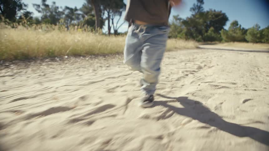 Little girl runs along a dirt road holding a yellow toy in a rural area with trees