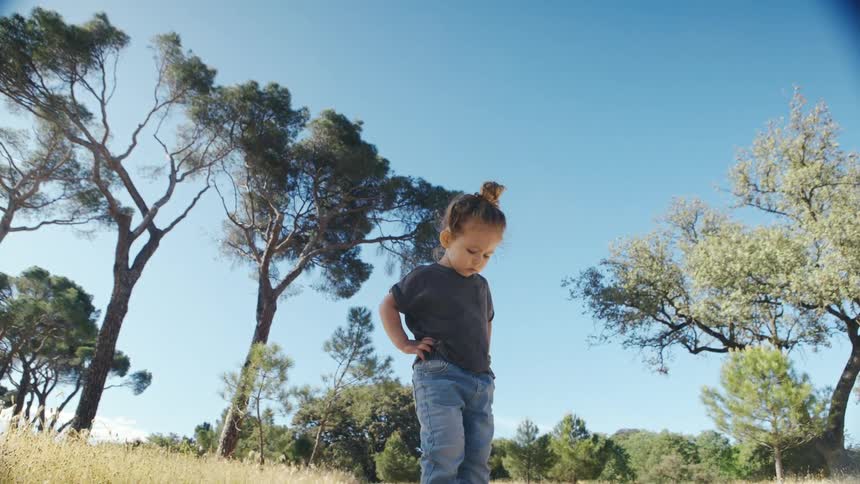 Little girl outdoors with her hand on her hip looking down