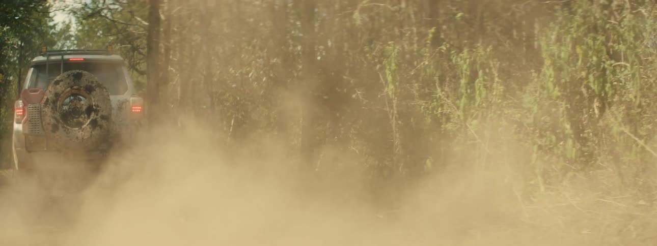 An suv driving through a forest on a dirt road as dust flies behind it as it moves