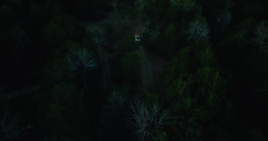 The truck is driving through the dark woods