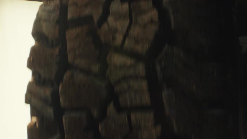 A close up shot shows a rugged offroad tire spinning rapidly as bright golden sunlight glows from the side highlighting the deep grooves and rough texture of the black rubber tread against a pale washed out background