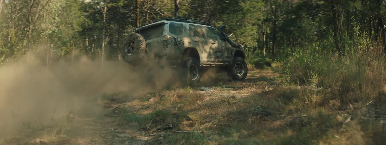 Jeep traveling on a dirt road through the woods leaving behind a trail of dust