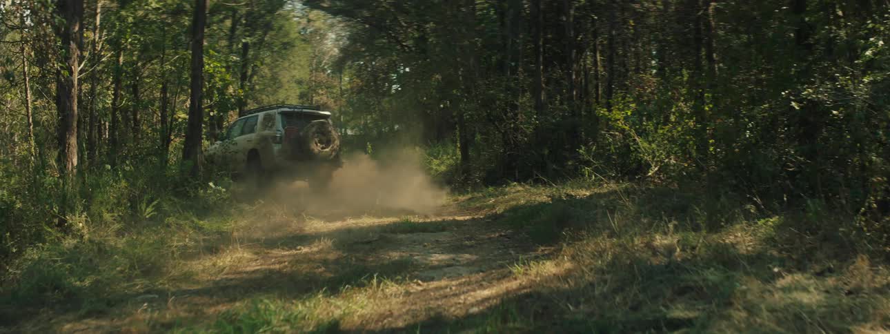 Pickup truck speeding down a forest trail kicking up dust
