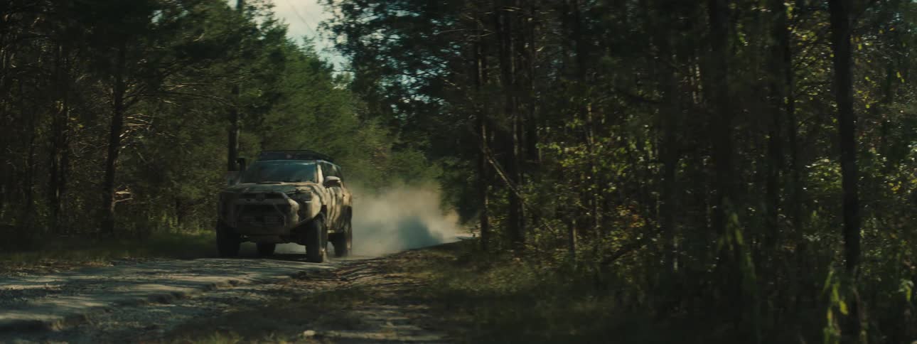 An suv speeds along a dusty dirt road through a dense forest kicking up a trail of dust behind it