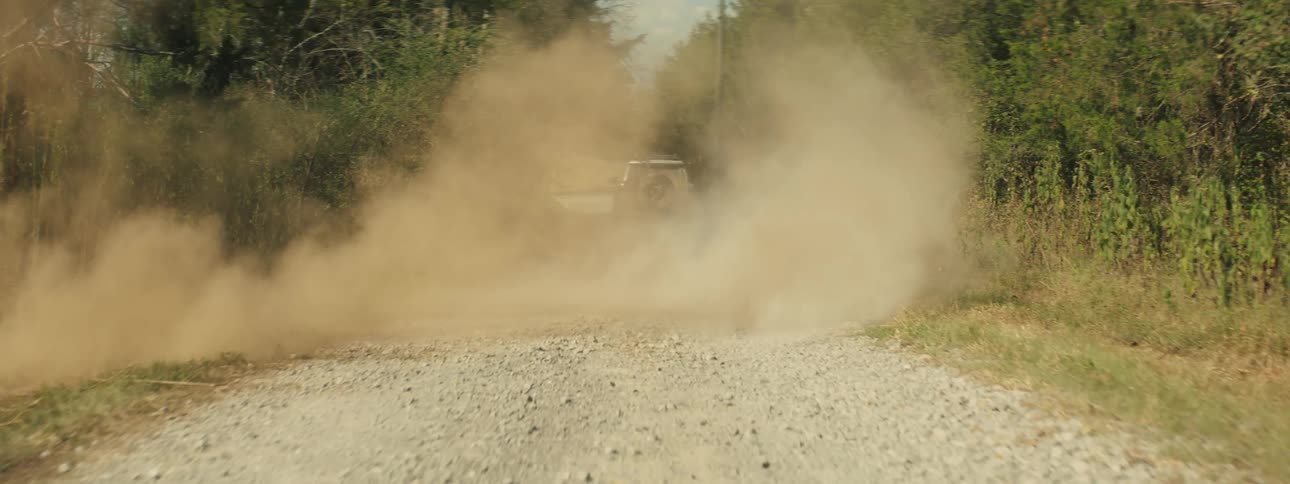 Suv raises a cloud of dust while driving along a dirt road between trees