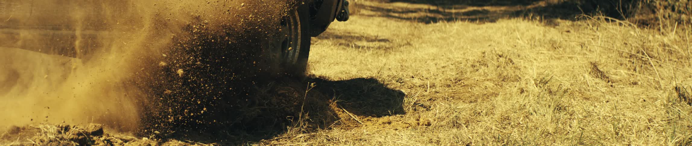 A close ground level view shows a tire spinning quickly and throwing a large amount of dirt and dust into the air as the vehicle begins to move across dry land