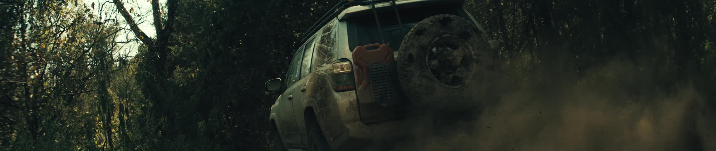 Mudcovered suv travels along a narrow trail between trees in a forest area