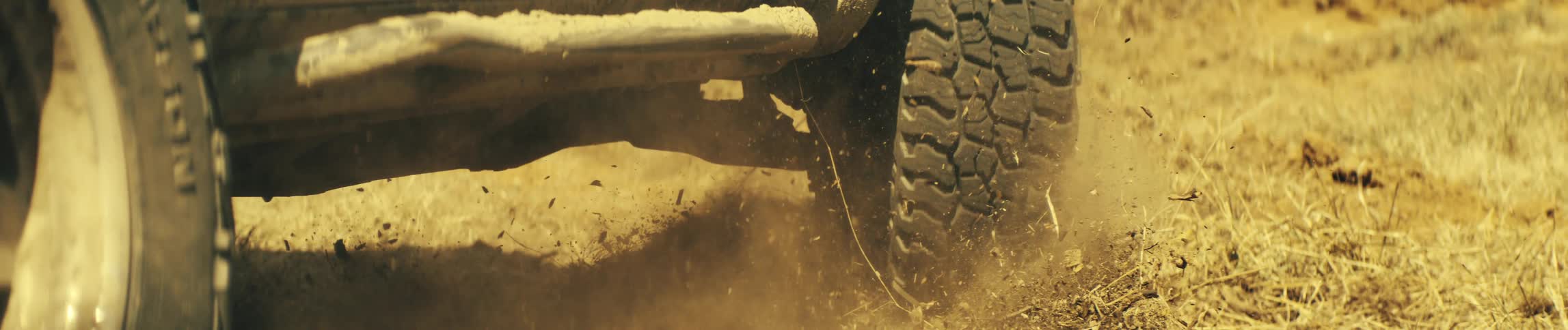 Truck tires turn as the vehicle moves over dry gras and dirt