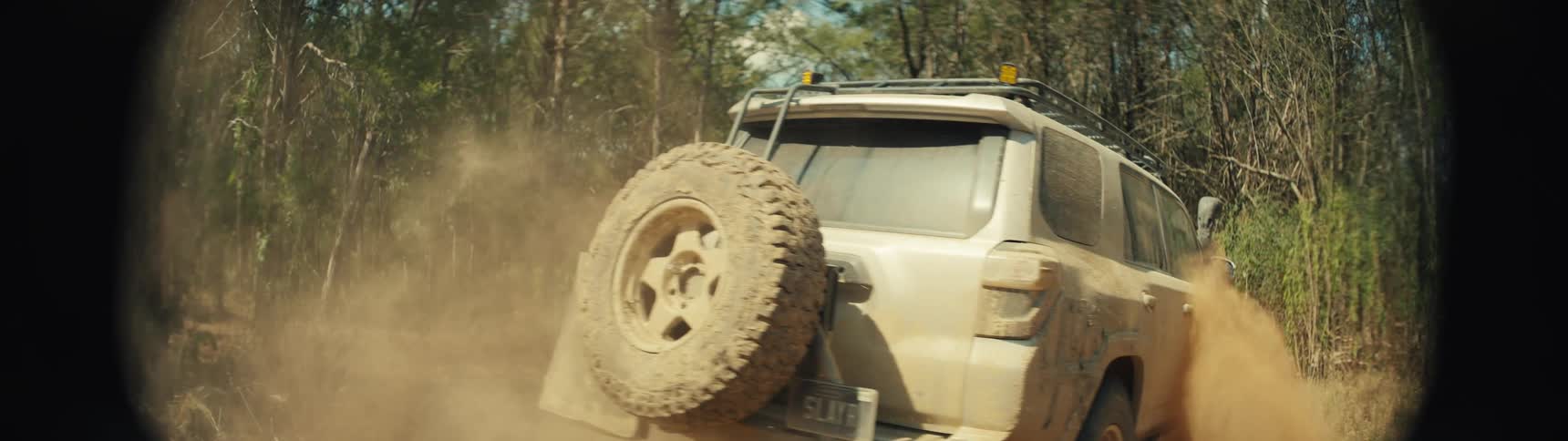 The truck leaves a dust cloud as it drives in the woods