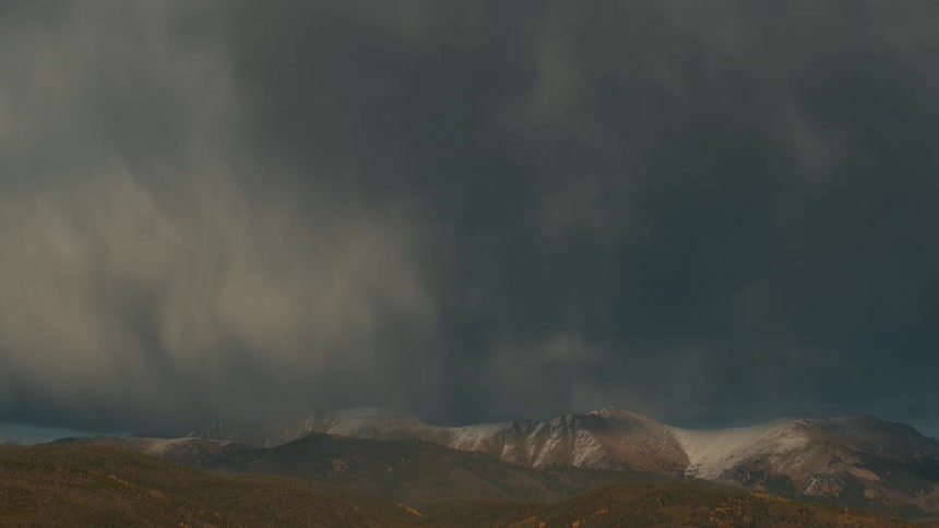 Dark heavy storm clouds loom over a distant mountain range during a moody sunset