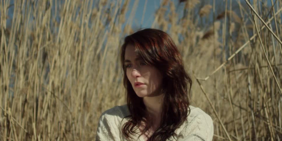 Dark haired woman closes eyes in a field