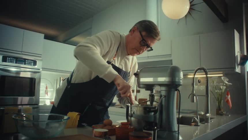 The man is cooking in the kitchen while using a mixer
