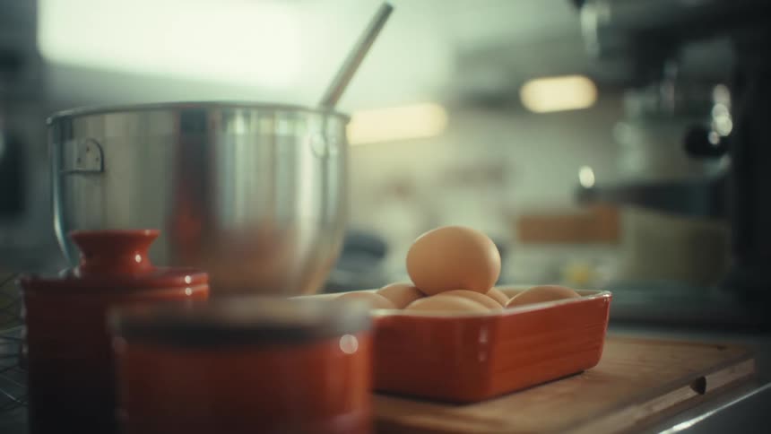 Baking ingredients including eggs in a dish and orange canisters sit on a counter next to a large metal mixing bowl