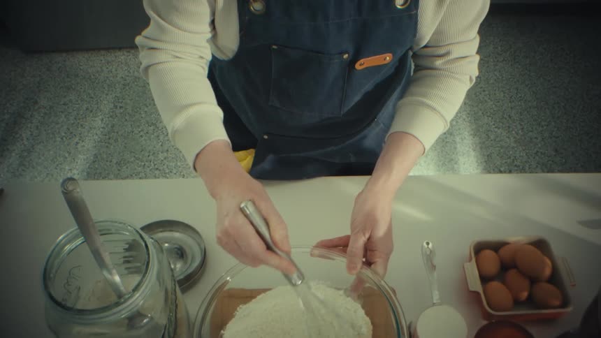 Hands use a whisk to mix flour in a bowl on a kitchen counter