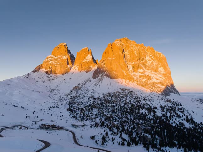 A snow covered mountain peak bathed in the warm light of sunset against a clear blue sky