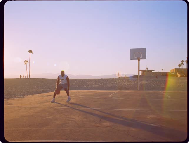 A man plays basketball on an outdoor court at the beach during a hazy sunset