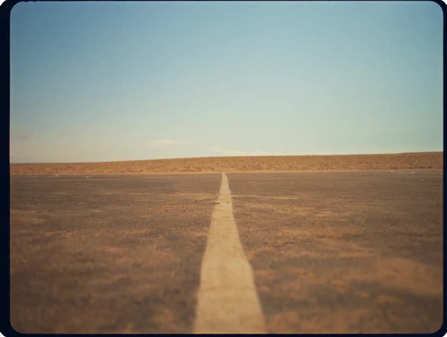A man drops into a crouched starting position to touch a white line on an outdoor track before exploding into a sprint and disappearing offscreen against a vast desert backdrop