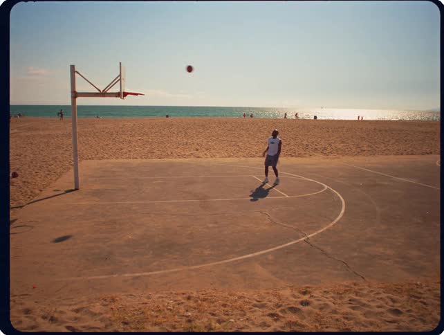 Person shooting a basketball on a beachside court with the ocean in the background