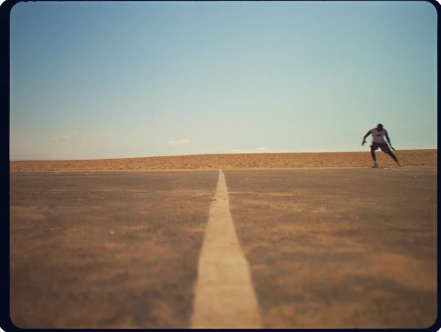 A runner sprints across an outdoor paved track in a desert environment
