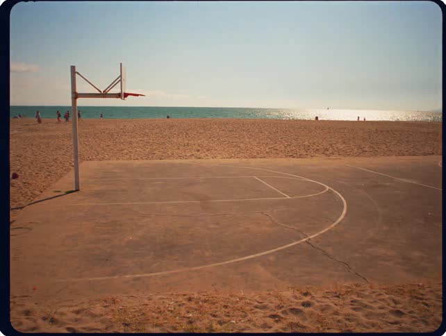 A man plays basketball on an outdoor court situated on a sandy beach next to the ocean