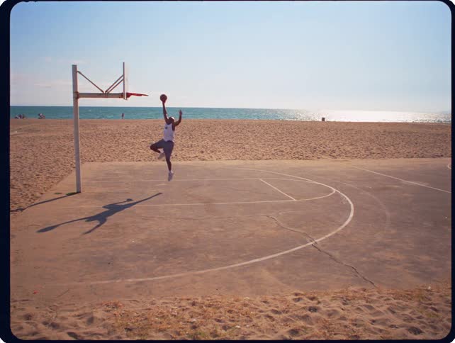 A man plays basketball on an outdoor court situated on a sandy beach