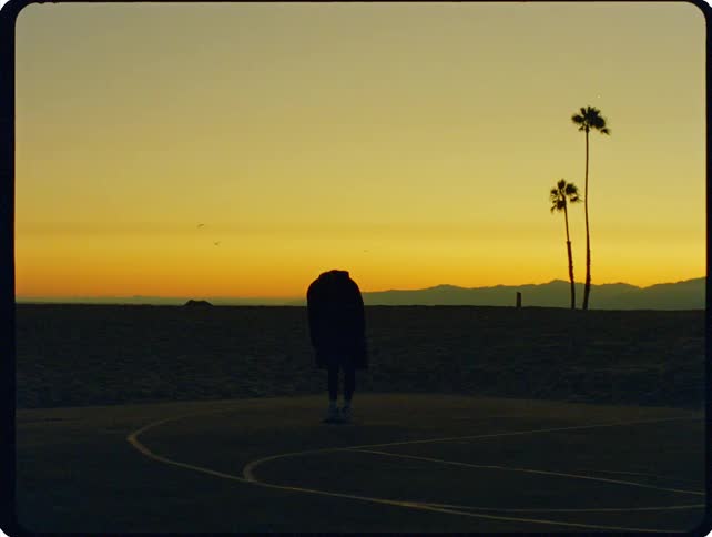 Person stretching on a beachside basketball court at sunset
