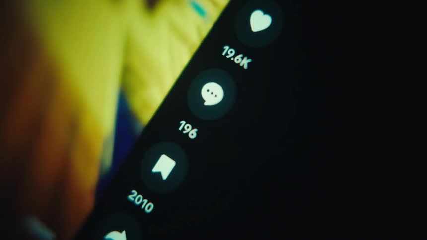 A person scrolls through a social media feed on a smartphone in a dark room