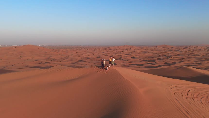 A group of people standing at the top of a dune in the desert