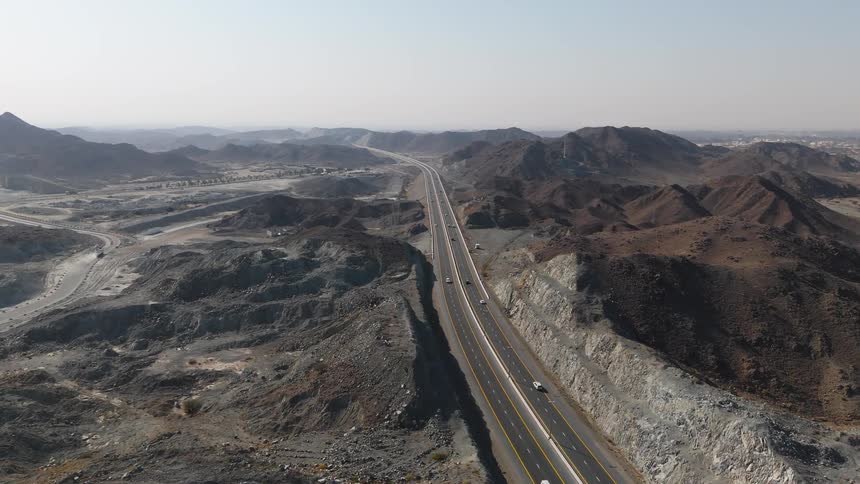 Highway crosses an arid mountainous region with vehicles moving along the road