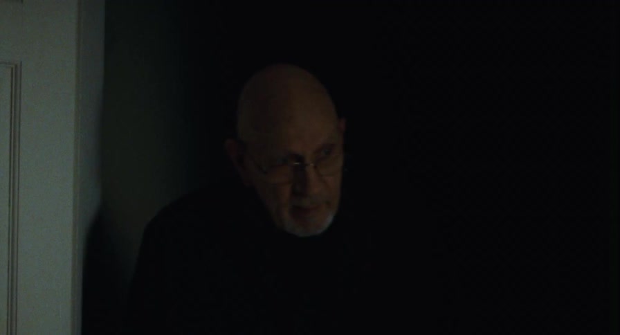 An old man stops in a doorway at night and lightly smiles