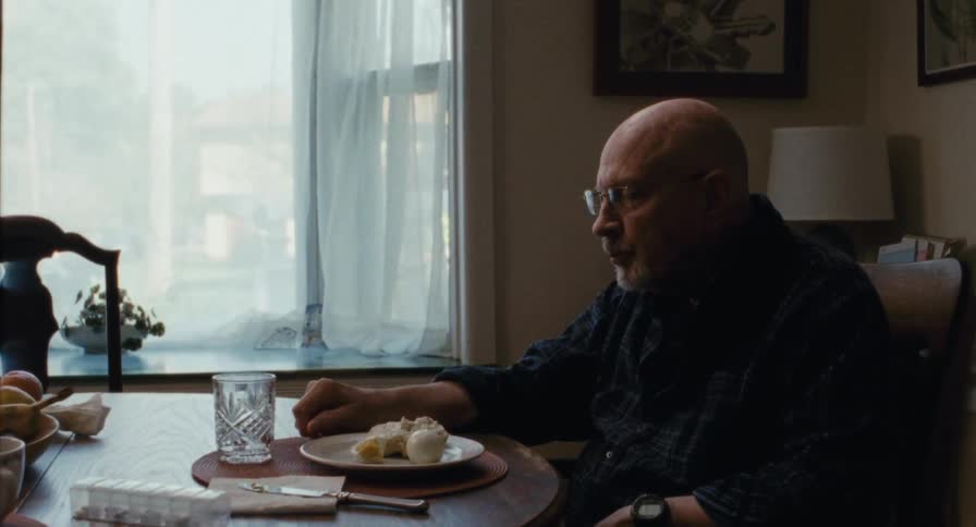 An old man takes a drink at the table while eating breakfast