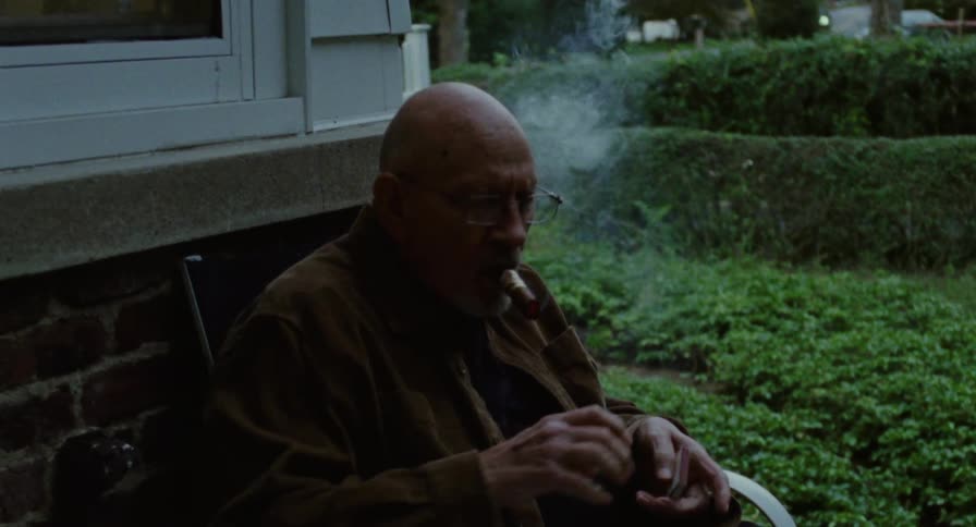 An elderly man lights and smokes a cigar outside