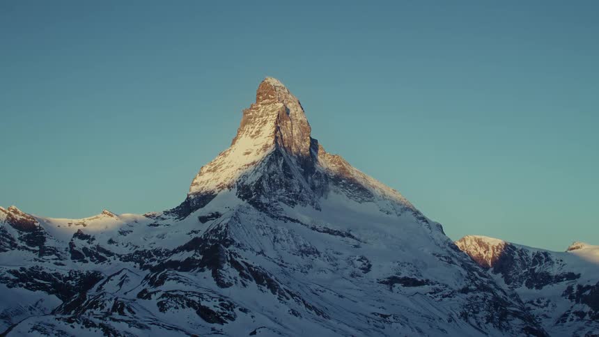 Snowcovered Matterhorn illuminated by sunlight against a blue sky