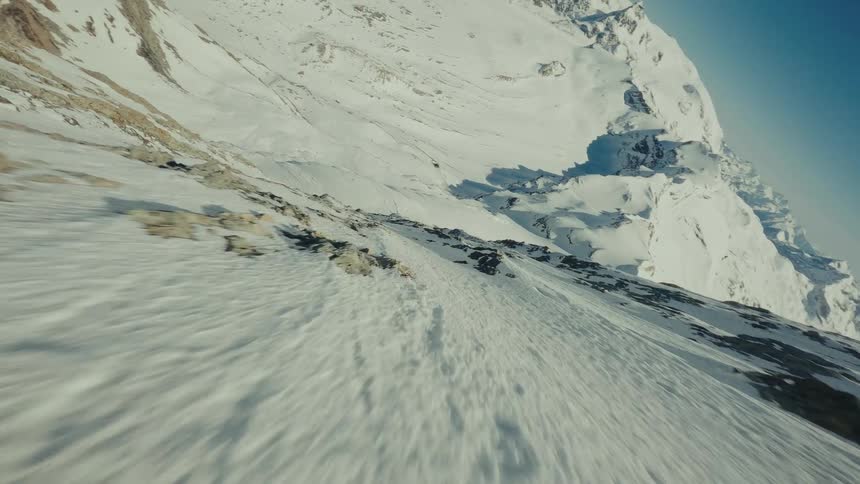 Moving over the rough terrain of a mountain slope with snow covered mountains in the distance