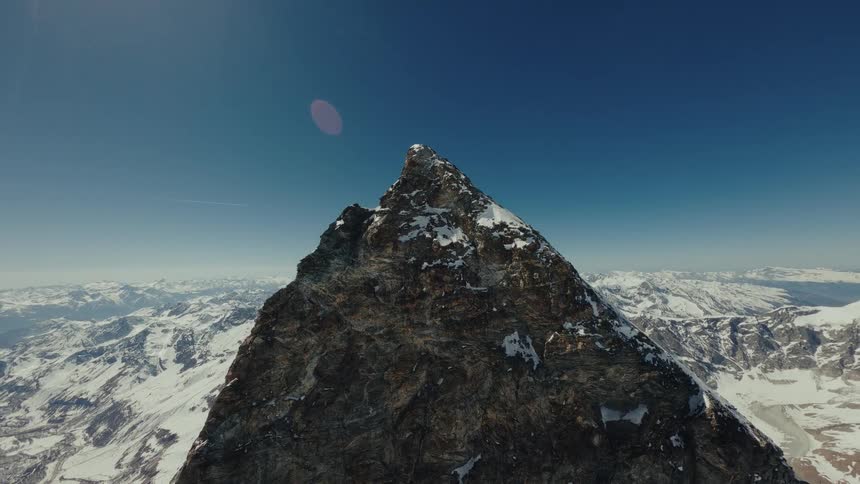 Rough terrain on a mountain with a pointed peak overlooking snow covered mountains across the landscape