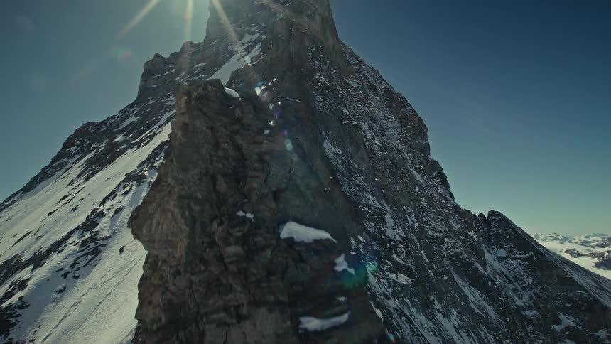 Moving over the rough terrain on a mountain ridge with snow on the slope as the sun shines brightly overhead