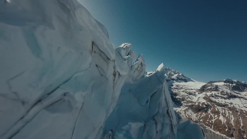 Jagged white glacial ice formations and steep snow covered ridges under a bright sun and clear blue sky