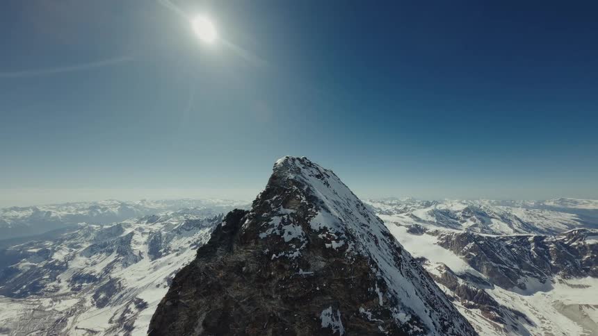 Rocky snowcovered peak under high sun above an extensive mountain range