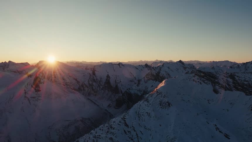 An aerial drone shot of snow covered mountain peaks during sunrise