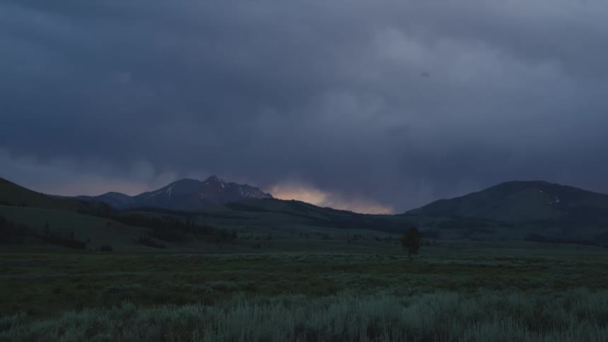 Trees and vegetation in the valley as dark clouds move over the mountains